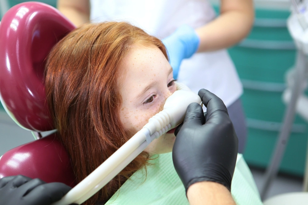 A young girl is being given inhalation sedation during dental treatment.